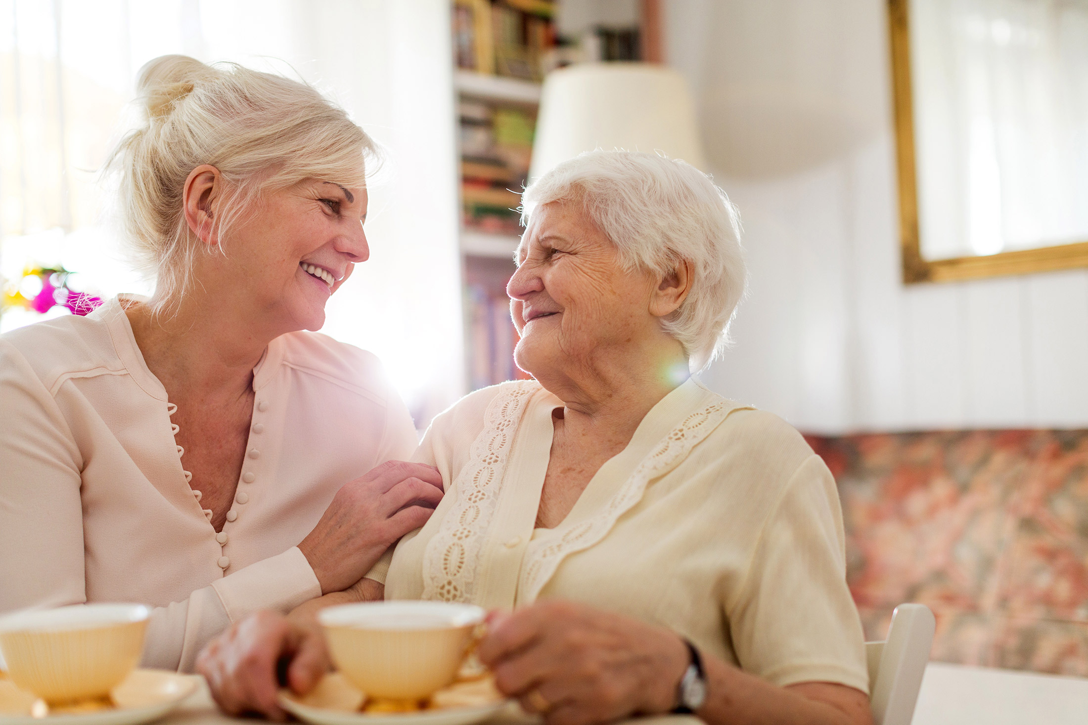 Two women smiling at each other with coffee mugs